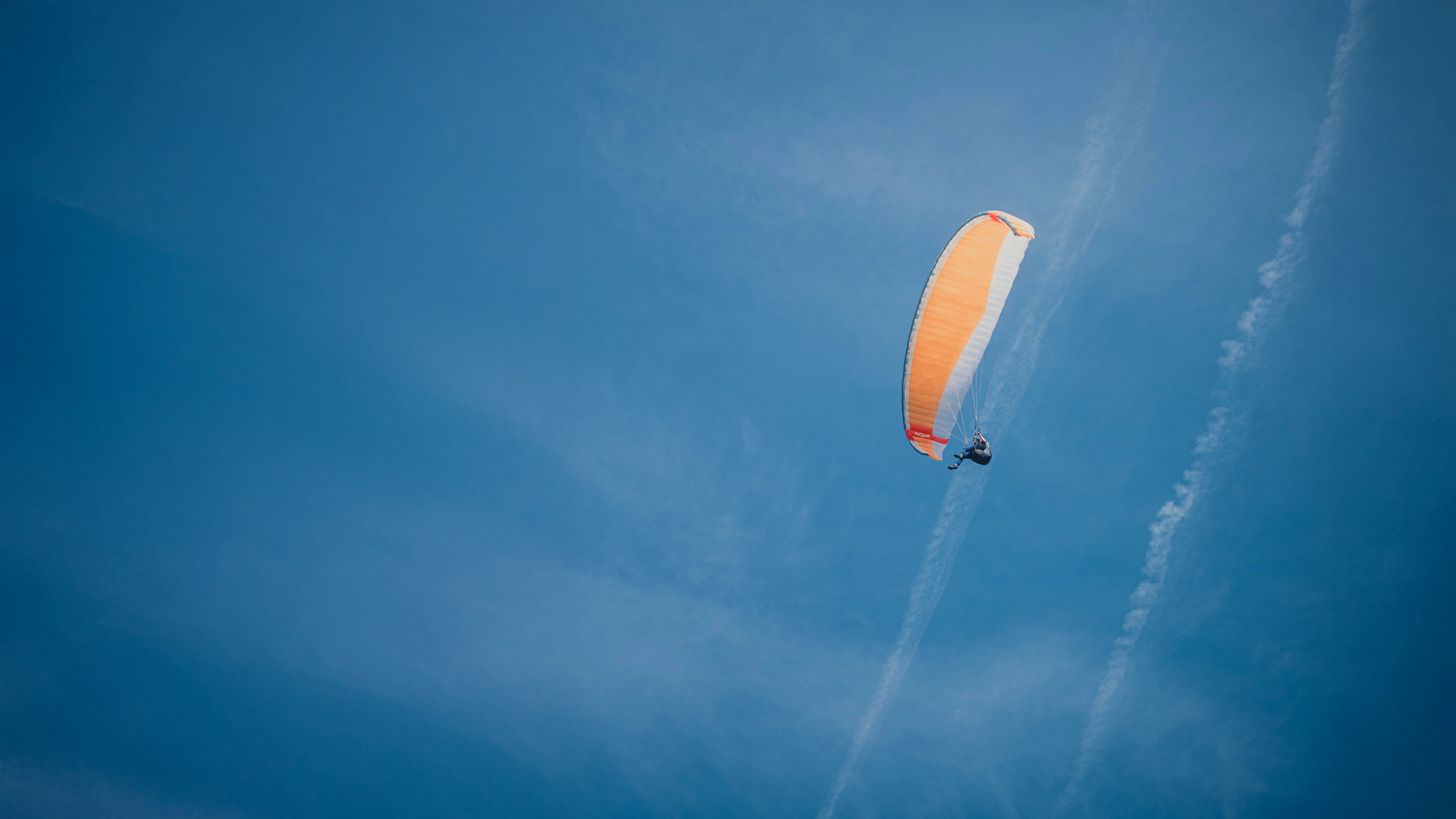 Orangener Gleitschirm fliegt vor blauem Himmel