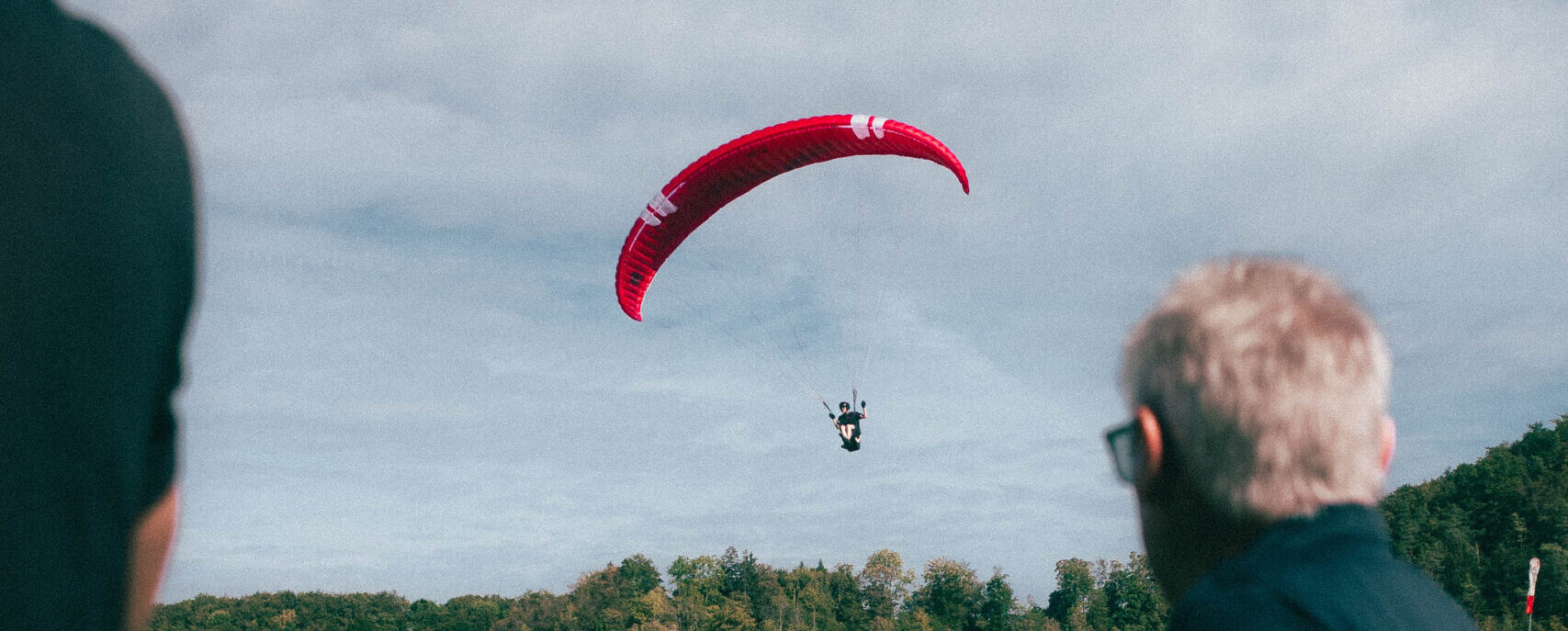 Roter Gleitschirm im Flug über Wiesen